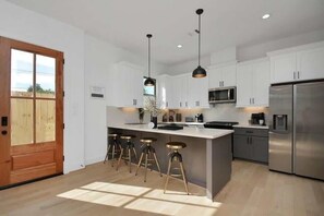 A modern kitchen with white cabinets, stainless steel appliances, and a central island with bar stools. - Pet-Friendly Midtown House, Private Yard & BBQ (Houston)