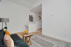 A modern living room with a dark green sofa, a small wooden table, and a patterned rug. - Pet-Friendly Midtown House, Private Yard & BBQ (Houston)