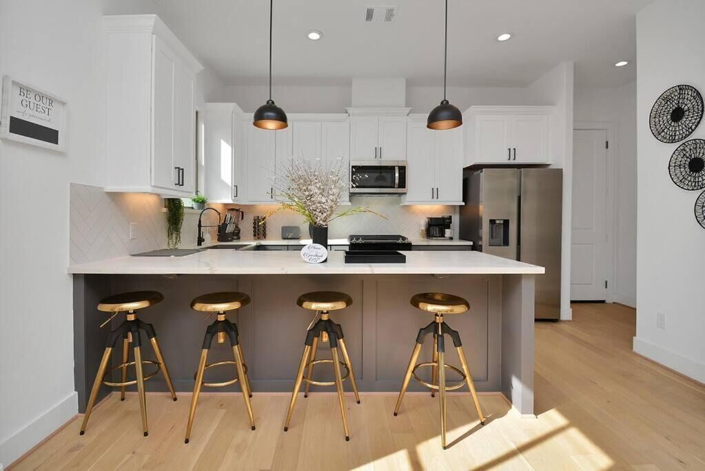 A modern kitchen with white cabinets, a central island with stools, pendant lighting, and a refrigerator.