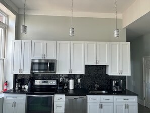 A modern kitchen with white cabinets, a black countertop, stainless steel appliances, and pendant lighting. - Huge Downtown home w/parking 4 bdrm Penn Station (Baltimore)