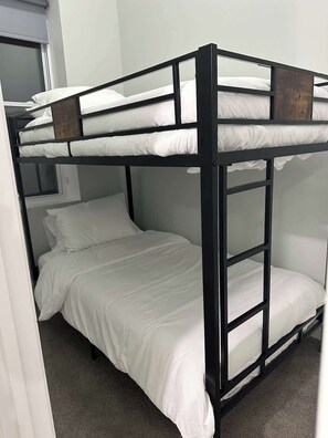 Ein Stockbett mit weißer Bettwäsche in einem Zimmer mit Teppichboden und einem Fenster.