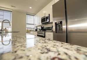 A modern kitchen with stainless steel appliances, a granite countertop, and white cabinetry. - Arts District Penthouse w/ Free Parking & 3 Baths (Baltimore)