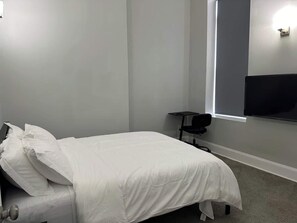 A single bed with white bedding in a room with a large window and a flat-screen TV mounted on the wall. - Arts District Penthouse w/ Free Parking & 3 Baths (Baltimore)