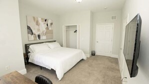 A bedroom with a bed, a desk, a chair, a wardrobe, a mirror, and a television. - Massive Downtown Penn Station apt with parking (Baltimore)