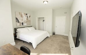 A bedroom with a bed, a desk, a chair, a wardrobe, a mirror, and a television. - Massive Downtown Penn Station apt with parking (Baltimore)