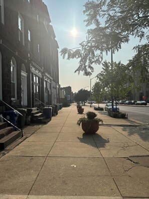 A street with a sidewalk, parked cars, and buildings with large windows. - Massive Downtown Penn Station apt with parking (Baltimore)