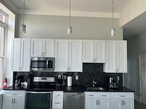 Une cuisine moderne avec des meubles blancs, un plan de travail noir, des appareils en acier inoxydable et des luminaires suspendus.