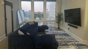 Ein Wohnzimmer mit großem Fenster, einer Sofagarnitur, einem Flachbildfernseher und einem Topfpflanzen.