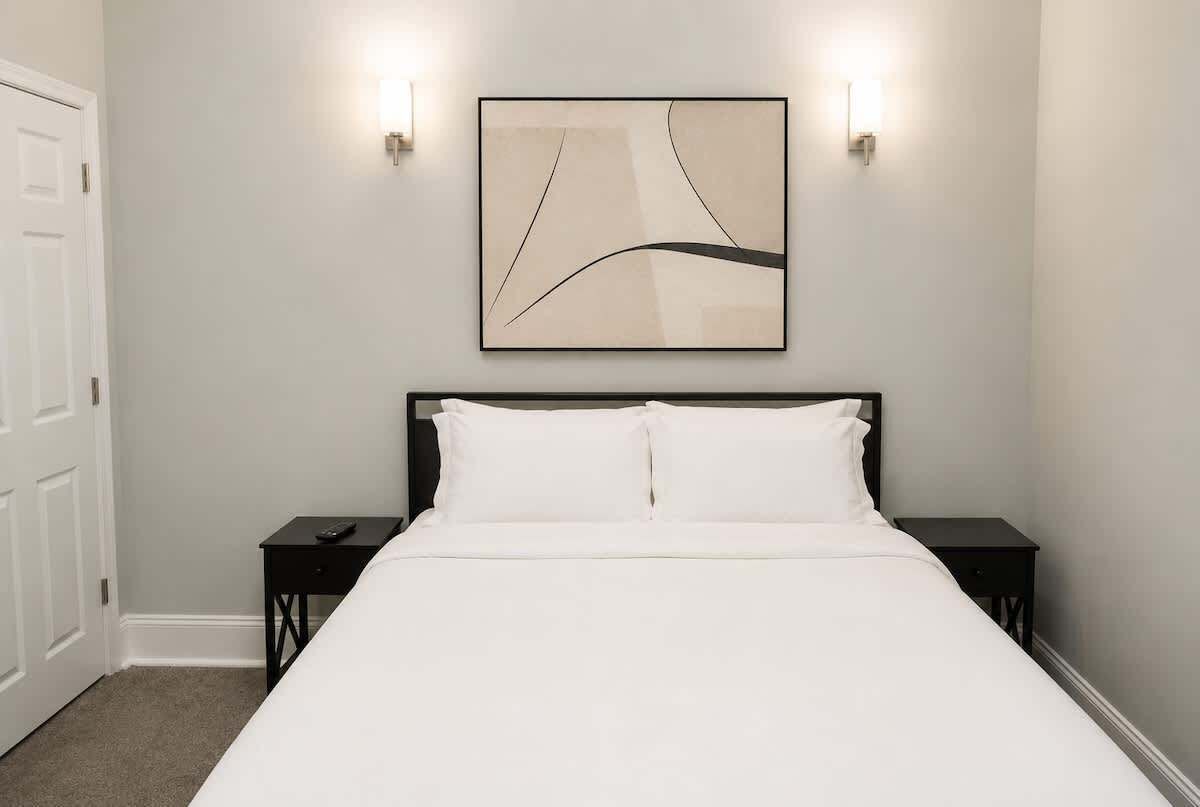 Een slaapkamer met een bed, twee nachtkastjes, een wandlamp en een abstract schilderij aan de muur.