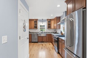 A modern kitchen with wooden cabinets, stainless steel appliances, and a window providing natural light. - Serenity Point- Shellcamp Lakefront- 4bd3.5bth-Mountain Views- Pet Friendly! (Gilmanton)