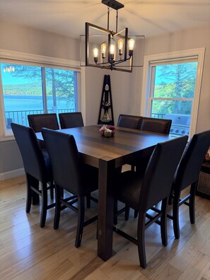 A dining area with a rectangular table, six chairs, a chandelier, and a view of a lake through large windows. - Serenity Point- Shellcamp Lakefront- 4bd3.5bth-Mountain Views- Pet Friendly! (Gilmanton)