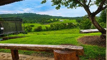 A rustic outdoor seating area with a bench, a metal grill, and a tree.