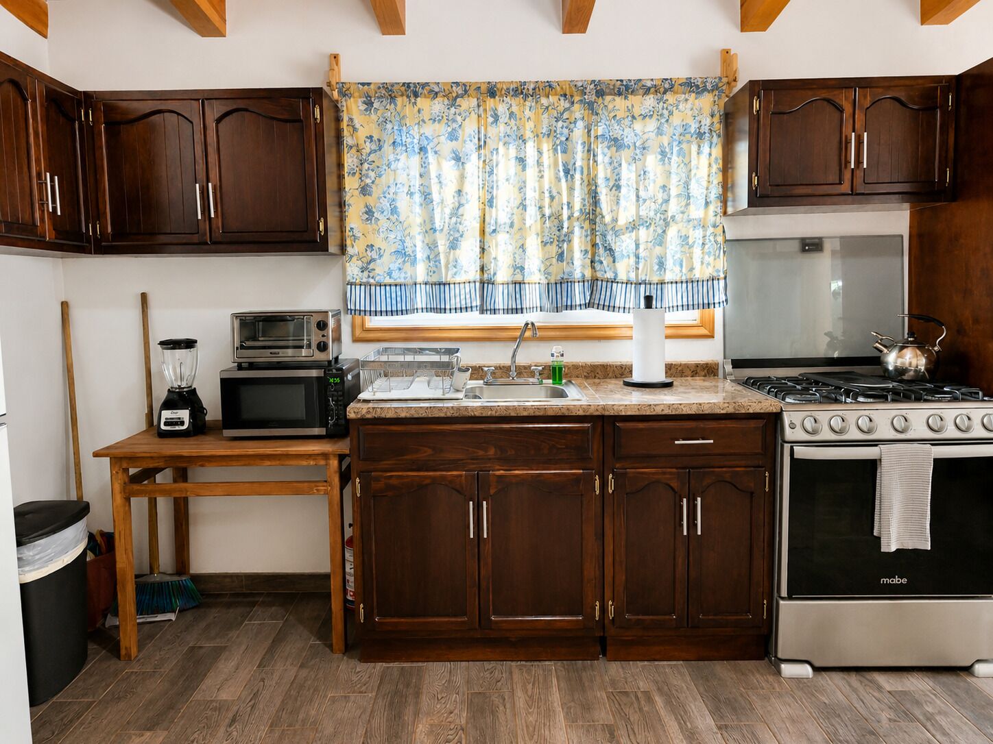 A kitchen with wooden cabinets, a stove, a microwave, and a blender on a wooden table.