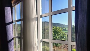 A room with a large window overlooking a garden and a hilly landscape.