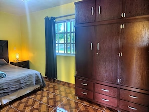Une chambre à coucher comprenant un lit, une table de chevet, une lampe, une fenêtre avec des rideaux et une armoire.