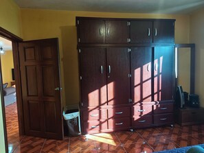 A room with a large wooden wardrobe, a bed with a blue cover, and a tiled floor.