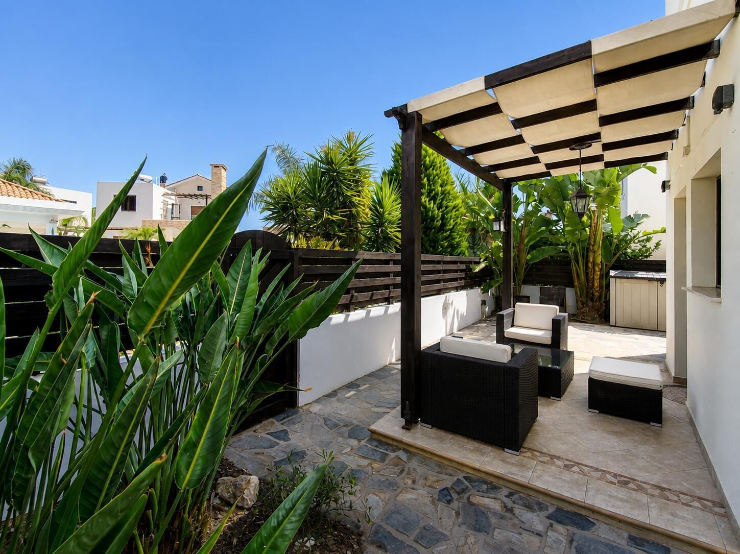 A patio area with outdoor furniture, a pergola, and tropical plants.