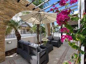 Un espace extérieur aménagé avec des meubles en osier, un grand parasol et des fleurs de bougainvillier.