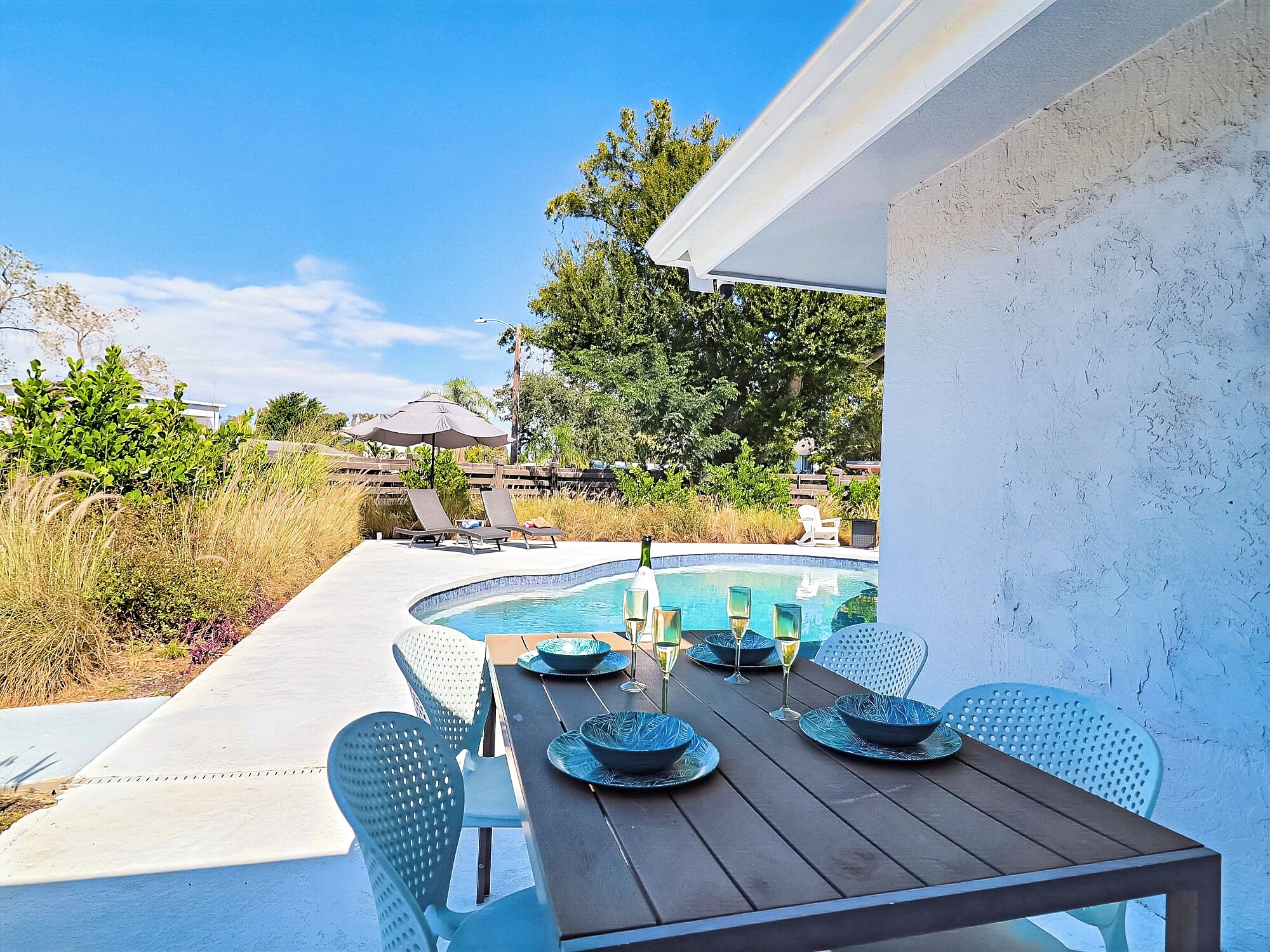 A poolside dining area with a table set for four, surrounded by chairs.
