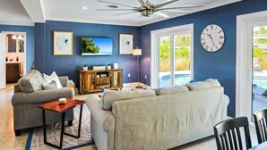 Un salon avec un ventilateur de plafond, une grande horloge et un téléviseur fixé au mur.