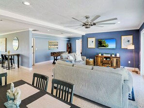 A spacious living room with a grey sofa, a coffee table, and a dining area with chairs and a table.