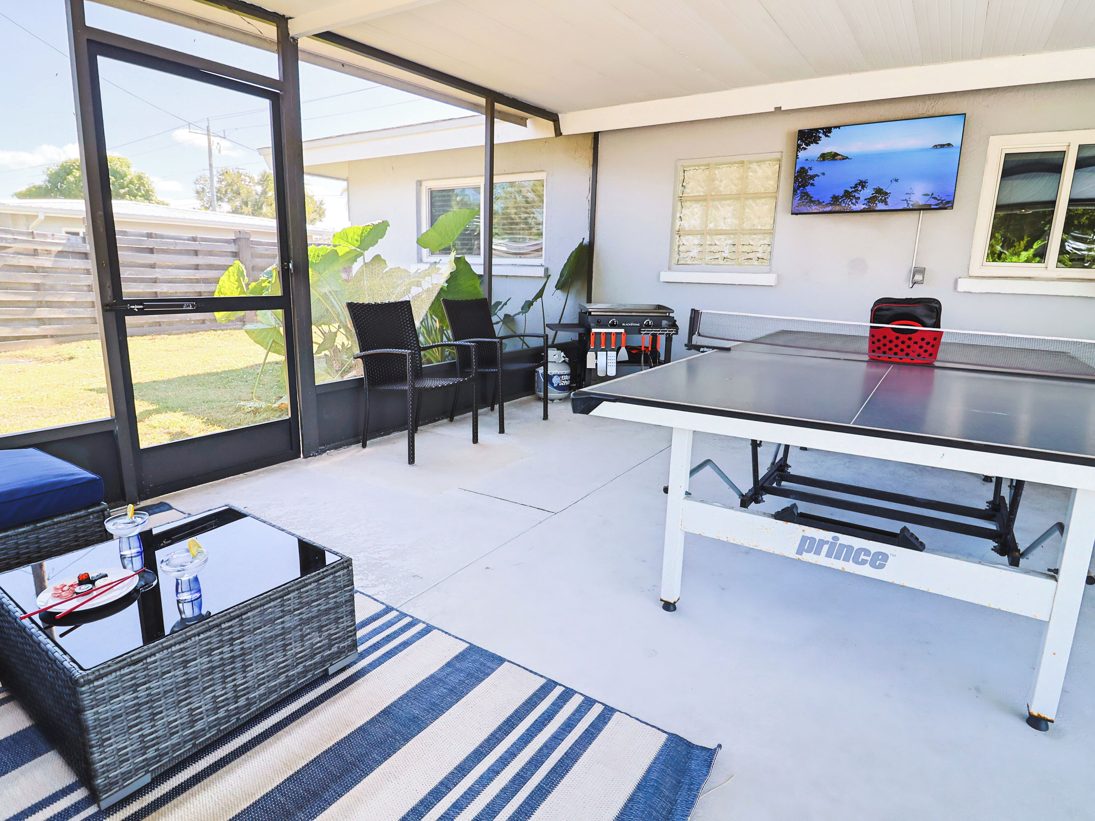 Une terrasse extérieure équipée d’une table de ping-pong, de chaises, d’une table en osier et d’un téléviseur fixé au mur.