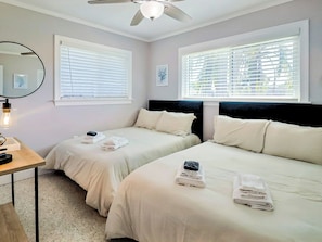 A hotel room with two beds, a ceiling fan, and two windows with blinds.