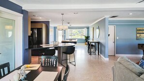 Une cuisine moderne dotée d’un îlot central, d’un coin repas avec une table et des chaises, et d’un salon avec un canapé.