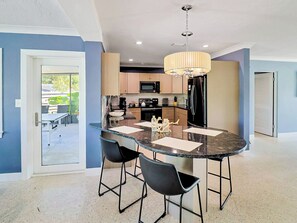 A modern kitchen with a central island, bar stools, and a chandelier.