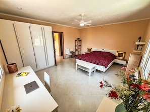 Quarto com cama, escrivaninha, cadeira e ventilador de teto.