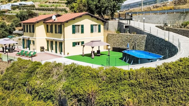 Un edificio de dos pisos con techo de tejas rojas, piscina y césped verde.