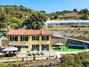 Um edifício de dois andares com telhado de telhas vermelhas, piscina e área de estar com espreguiçadeiras.