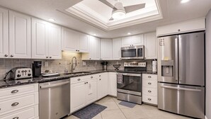 A modern kitchen with white cabinetry, stainless steel appliances, a ceiling fan, and a skylight. - 1200-406 - Standard Plus - Embrace Spectacular Water Views (Siesta Key)
