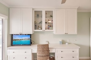 Ein Zimmer mit weißem Schreibtisch, einem Fernseher, der eine schöne Aussicht zeigt, und einem Korbstuhl.