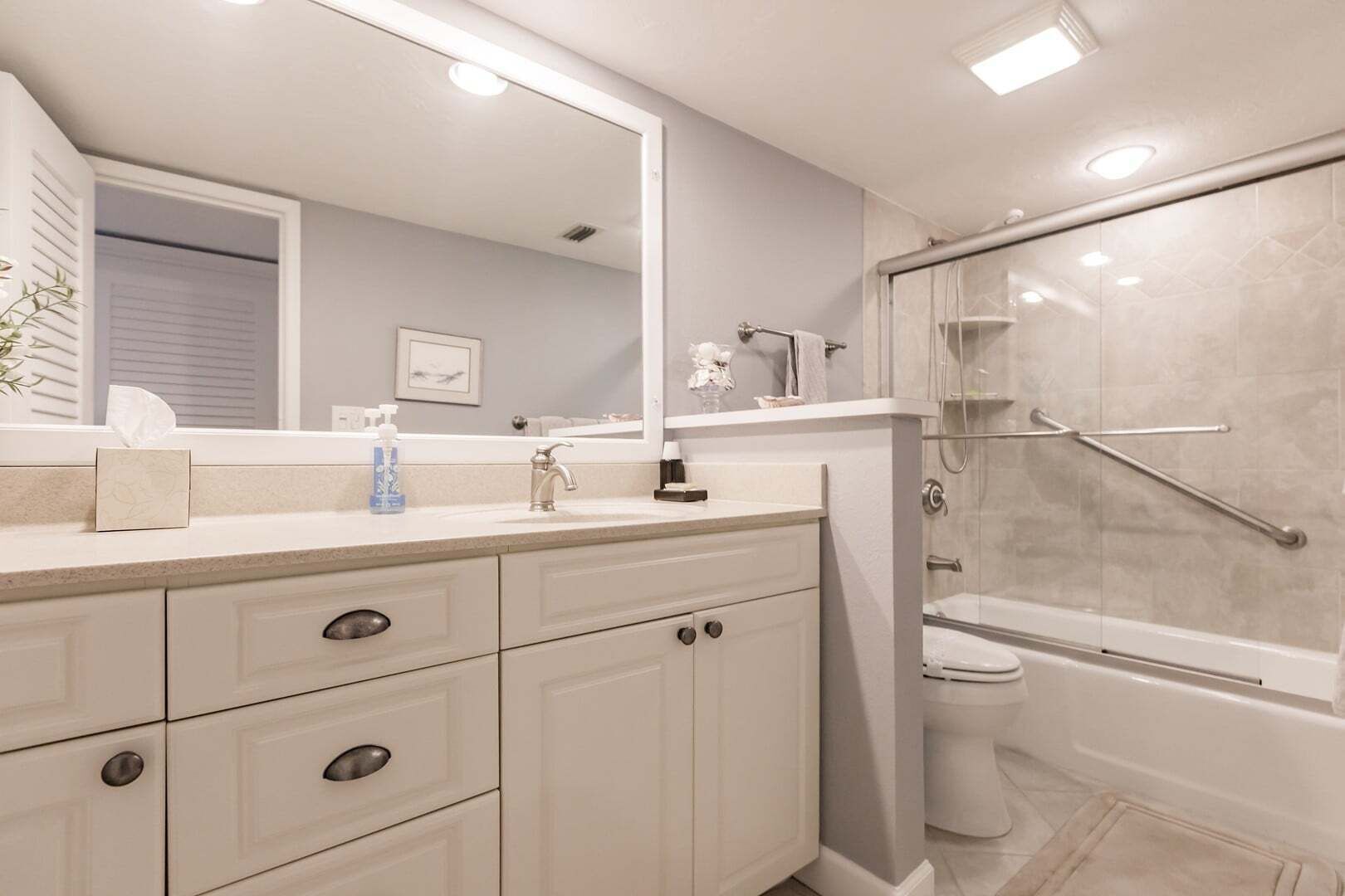 Un bagno con uno specchio grande, un lavandino, un water e una doccia.