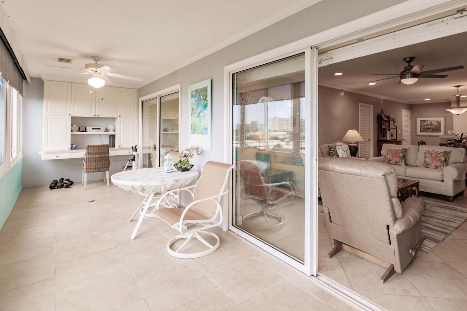A spacious living area with a sliding glass door leading to a balcony, a dining area with a round table and chairs, and a kitchen with white cabinets.