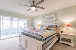 Ein Schlafzimmer mit einem Bett, einem Deckenventilator, einem Nachttisch mit Lampe und einem großen Fenster.
