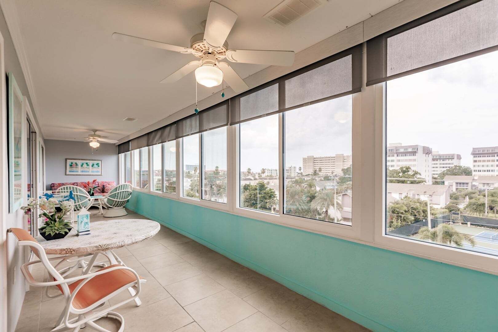 Un balcon avec vue sur la ville, un ventilateur de plafond et un coin salon avec des chaises et une table.