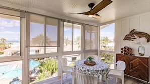 A sunlit room with a view of a pool and palm trees, a ceiling fan, and a table with chairs. - 6018 - Gulfside Oasis with a beach view (Siesta Key)