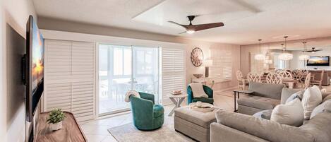 A spacious living room with a large TV, comfortable seating, a ceiling fan, and a view through the sliding glass doors.