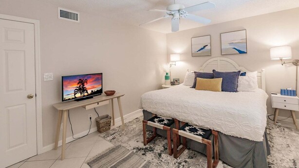 A bedroom with a bed, bedside tables, a television, a ceiling fan, and artwork on the walls. - 6018 - Gulfside Oasis with a beach view (Siesta Key)