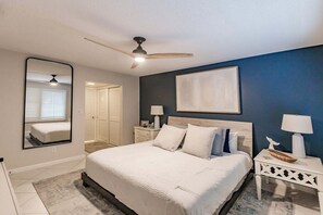 Ein Schlafzimmer mit einem Bett, Nachttischen, einem Deckenventilator, einem Spiegel und einer Tür.