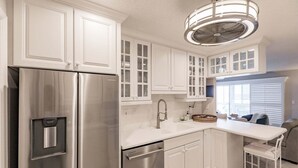 A modern kitchen with white cabinetry, stainless steel appliances, and a built-in island with seating. - 6018 - Gulfside Oasis with a beach view (Siesta Key)