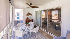 A covered outdoor dining area with a table and chairs, a ceiling fan, and a view of the beach through large sliding glass doors. - 6018 - Gulfside Oasis with a beach view (Siesta Key)