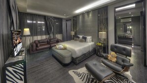 Una camera d'hotel moderna con un letto grande, un divano, una poltrona e un tavolino con un orsacchiotto.