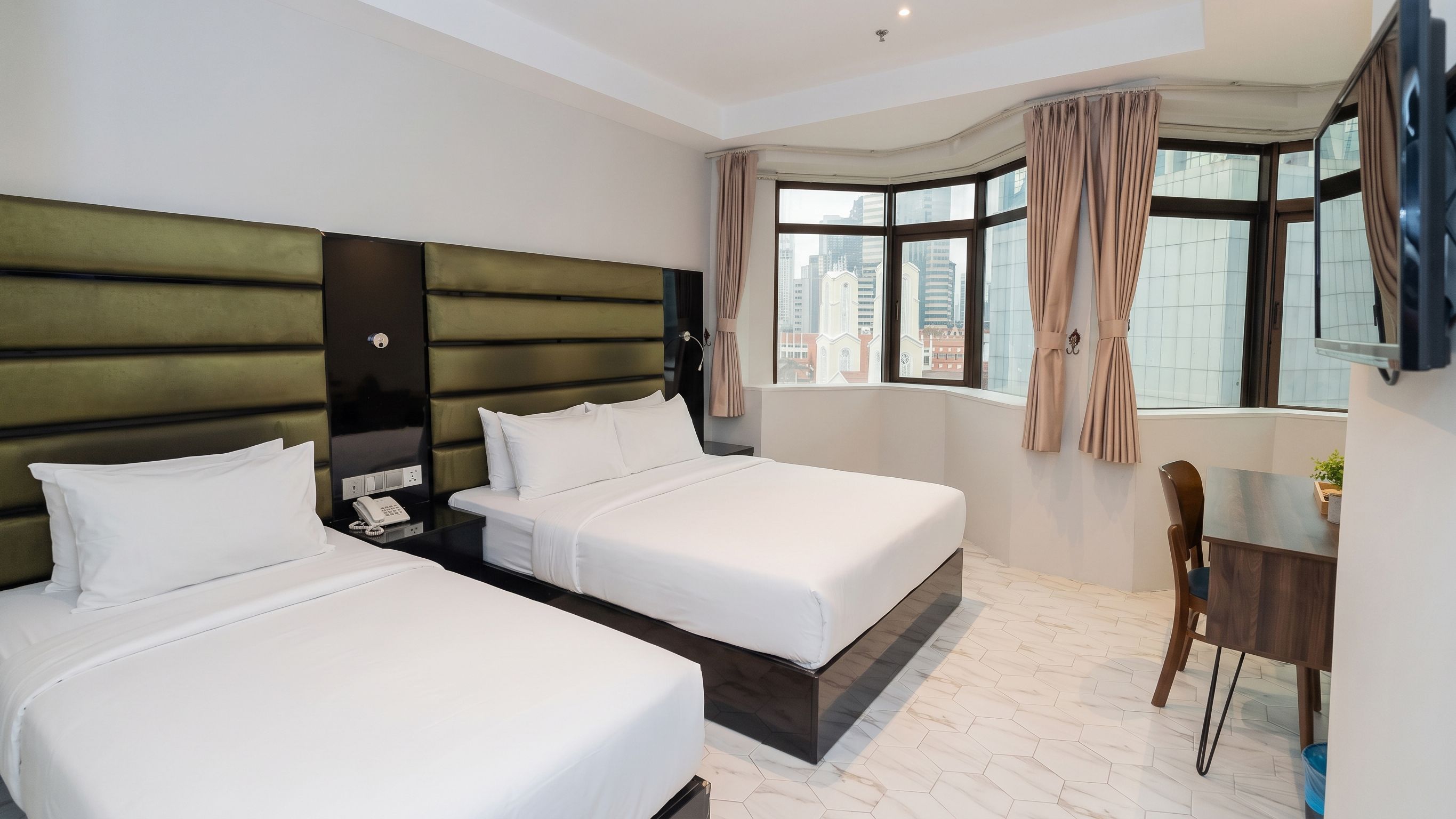 A hotel room with two beds, a desk, and a view of the city.