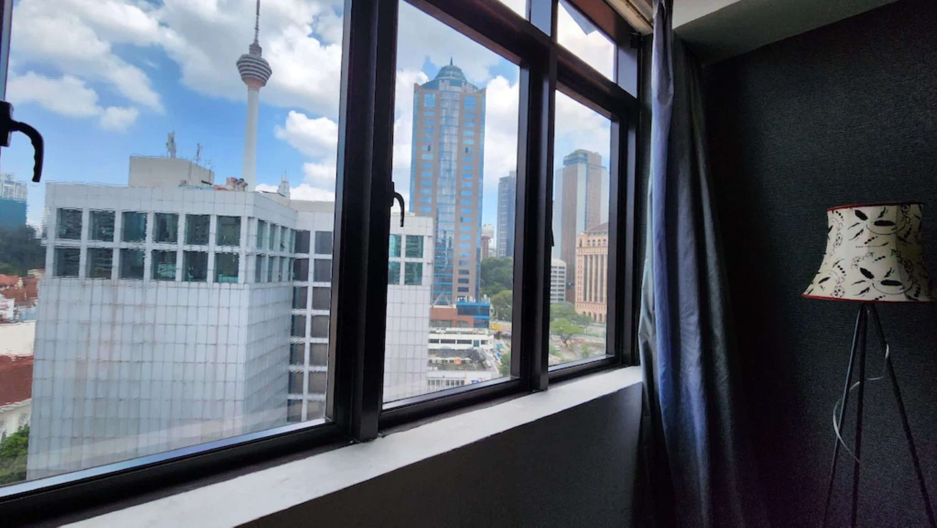 Una habitación con un ventanal grande que da a una vista urbana, incluyendo una torre y varios edificios altos.