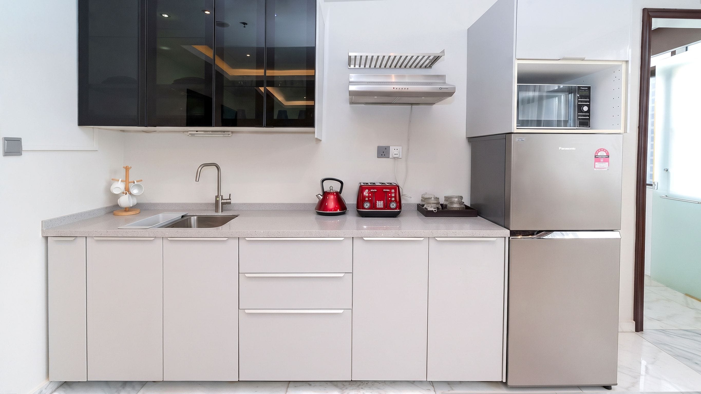 Una cocina moderna con un refrigerador de acero inoxidable, horno empotrado y una tetera sobre la encimera.