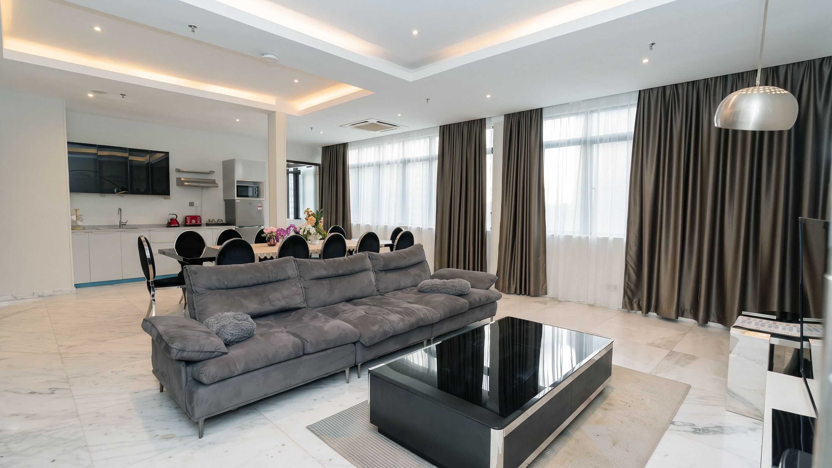 Una sala de estar moderna con un sofá gris, una mesa de centro negra y un comedor con mesa y sillas.