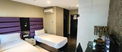 A hotel room with two beds, a desk, and an air conditioning unit.